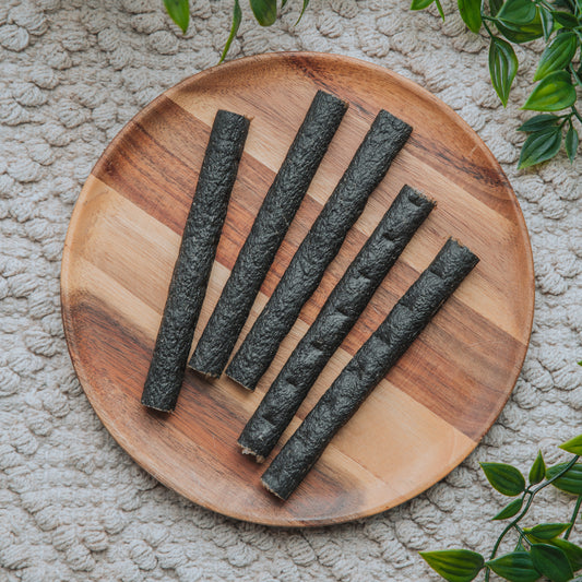 Wooden plate with black rolled snacks on a textured surface with green leaves.